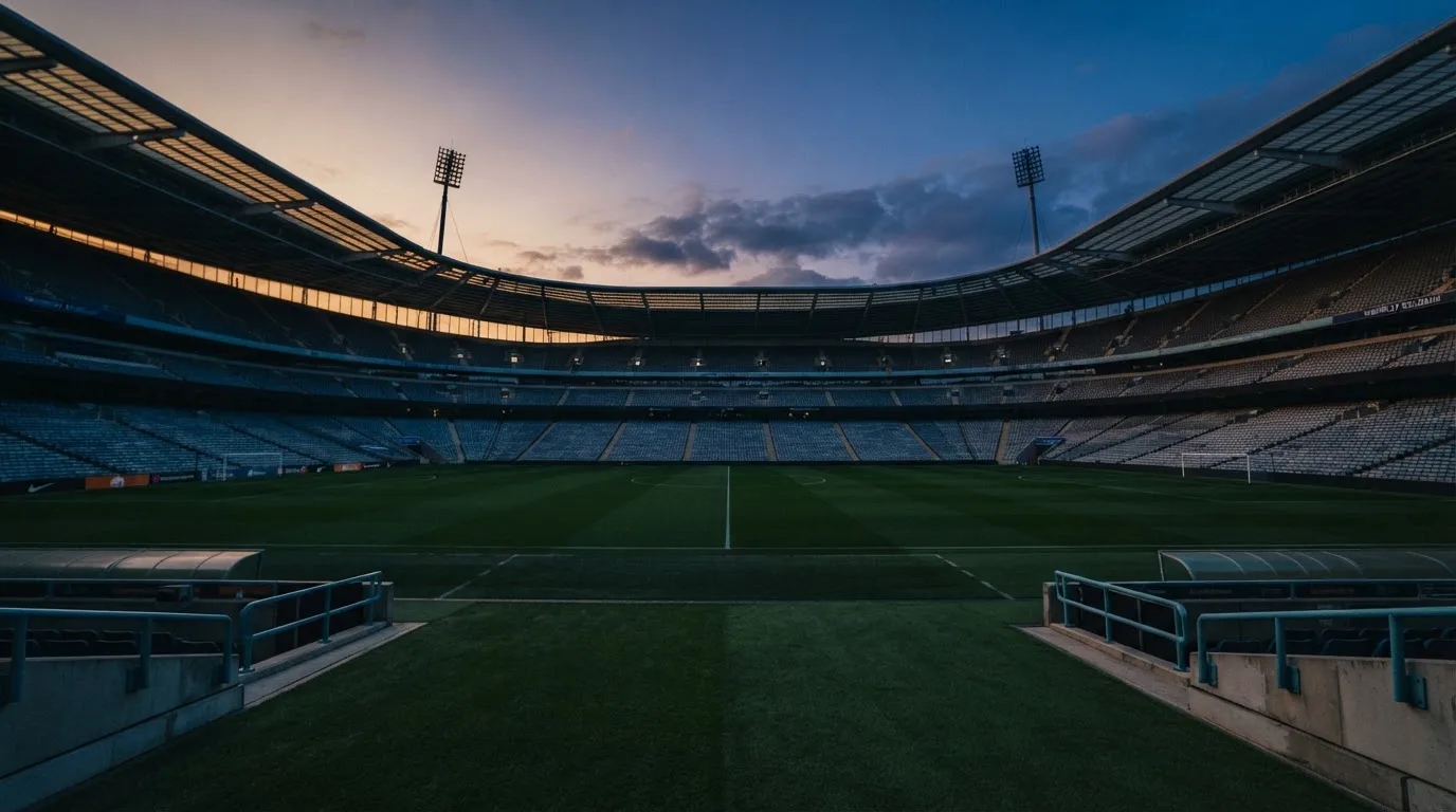 An empty football stadium with floodlight masts at dusk