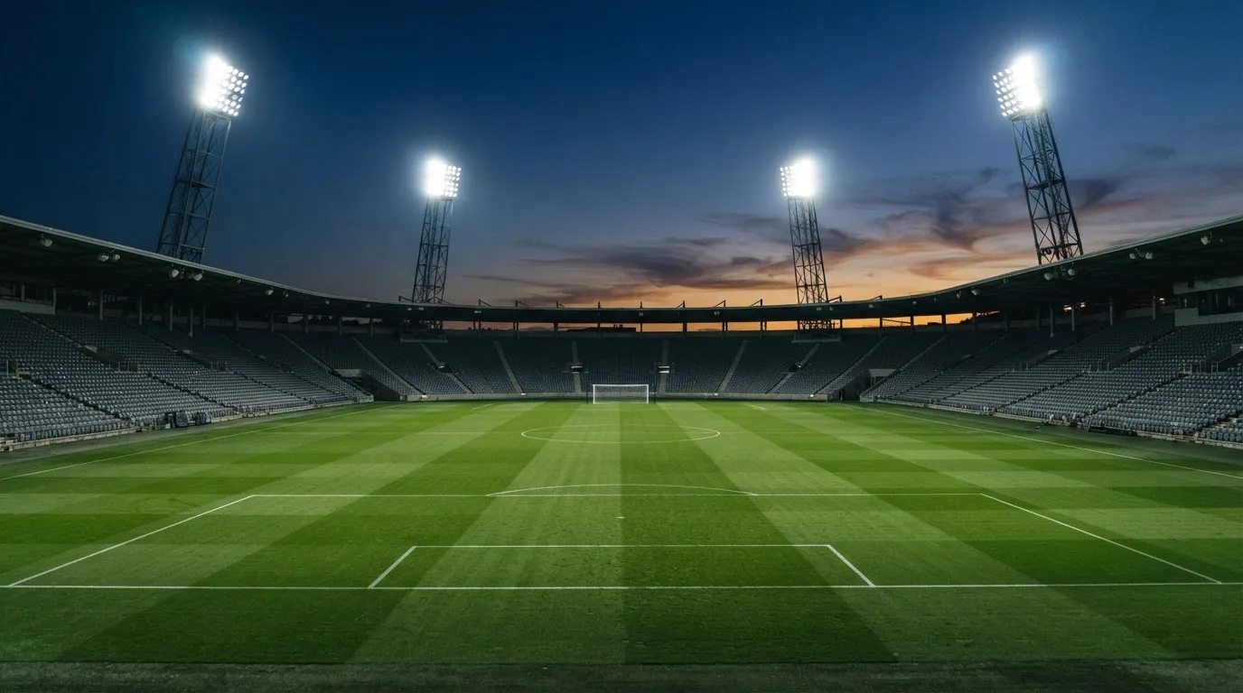 An empty football stadium with floodlight masts at dusk